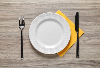 Plate with shiny silver fork and knife on wooden table, flat lay