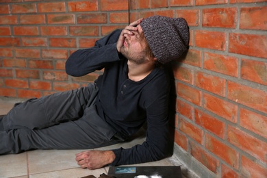Young addicted man sitting near brick wall after using drugs
