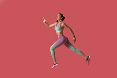 Athletic young woman running on pink background, side view