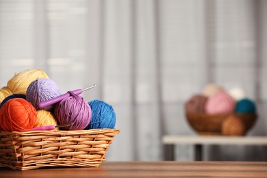 Wicker basket with clews of colorful knitting threads and crochet hooks on wooden table indoors. Space for text