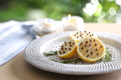 Lemons with cloves and fresh rosemary on wooden table outdoors, closeup. Natural homemade repellent