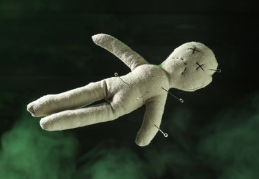 Voodoo doll with pins and smoke on dark green background