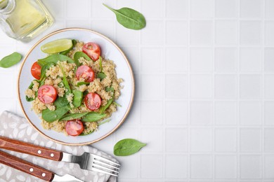 Photo of Delicious quinoa salad with tomatoes and spinach leaves served on white tiled table, flat lay. Space for text
