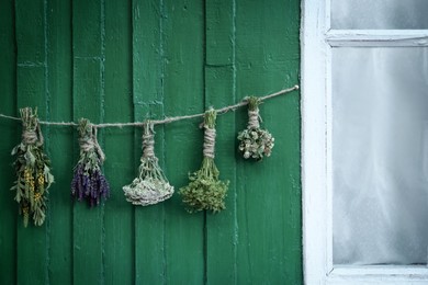 Bunches of different beautiful dried flowers hanging on rope near green wooden wall outdoors