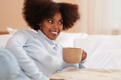 Photo of Smiling African American woman with cup of drink on bed at home. Space for text
