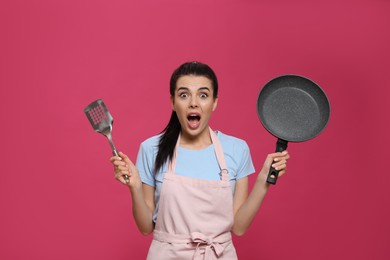 Emotional housewife with frying pan and spatula on pink background