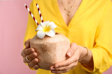 Woman holding fresh young coconut with straws on pink background, closeup