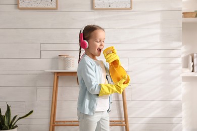 Cute little girl in headphones with bottle singing while cleaning at home