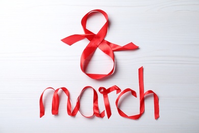 Photo of 8 March greeting card design with red ribbon on white wooden background, flat lay. International Women's day