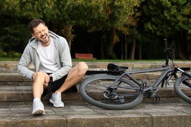 Man with injured knee on steps near bicycle outdoors