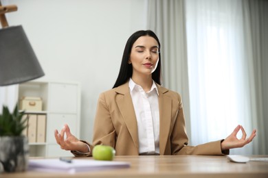 Young woman meditating at workplace. Stress relief exercise