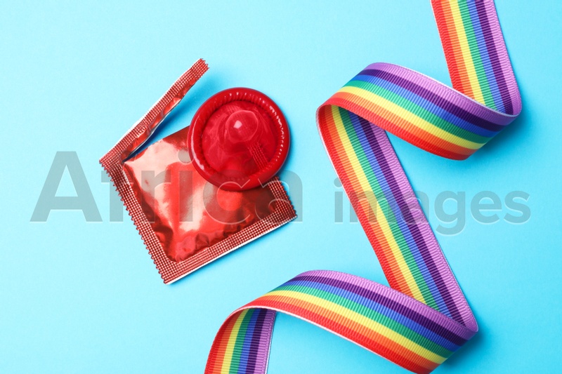 Red condom and rainbow ribbon on light blue background, flat lay. LGBT concept