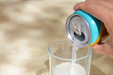 Woman pouring drink from aluminum can into glass at table, closeup. Space for text