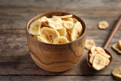 Bowl and spoon with sweet banana slices on wooden table. Dried fruit as healthy snack