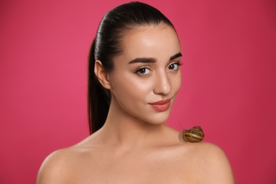 Beautiful young woman with snail on her shoulder against pink background