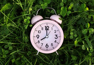 Pink small alarm clock on green grass outdoors, top view