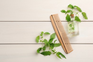 Stinging nettle, extract and comb on white wooden background, flat lay with space for text. Natural hair care
