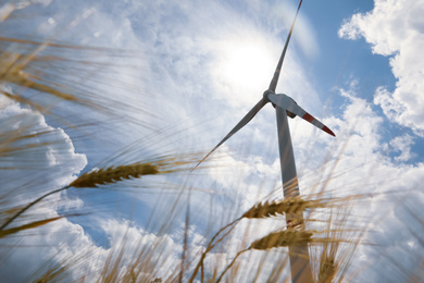 Modern wind turbine and wheat against cloudy sky, low angle view. Alternative energy source