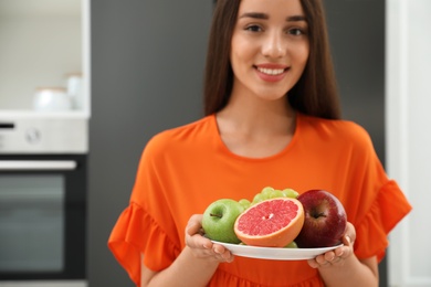 Photo of Concept of choice between healthy and junk food. Woman holding fruits near refrigerator in kitchen, focus on plate