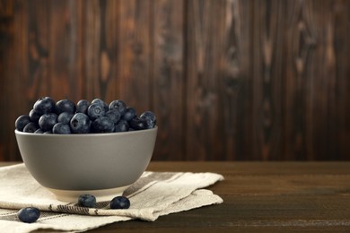 Ceramic bowl with blueberries on wooden table, space for text. Cooking utensil