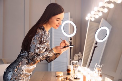 Young woman applying make up near illuminated mirror indoors