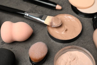Composition with skin foundation, powder and beauty accessories on grey background