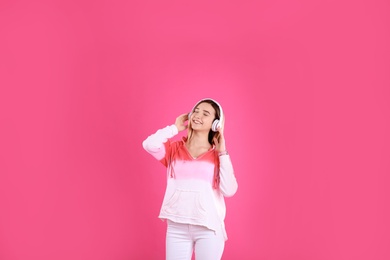 Teenage girl listening to music with headphones on color background