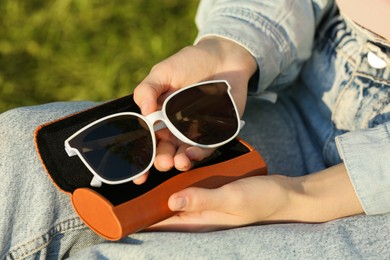 Woman holding sunglasses in brown leather case outdoors on sunny day, closeup