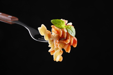 Delicious fusilli pasta with tomato sauce on fork against  black background