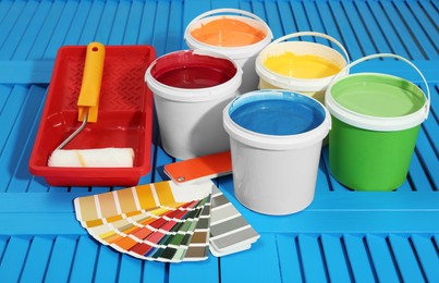 Buckets of paints, palette and decorator's tools on light blue wooden background