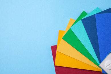 Multicolored paper sheets and space for text on light blue background, flat lay. Rainbow palette