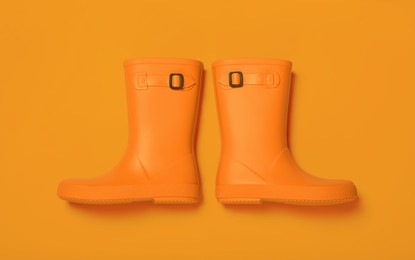 Pair of bright rubber boots on orange background, top view