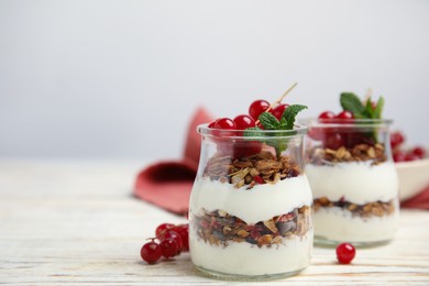 Delicious yogurt parfait with fresh red currants and mint on white wooden table, space for text