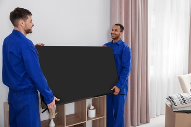 Photo of Male movers installing plasma TV near white wall in new house