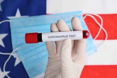 Scientist holding test tube with blood sample over American flag, closeup. Coronavirus pandemic in USA