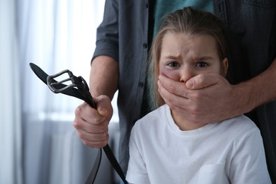Photo of Man with belt covering scared little girl's mouth indoors. Domestic violence