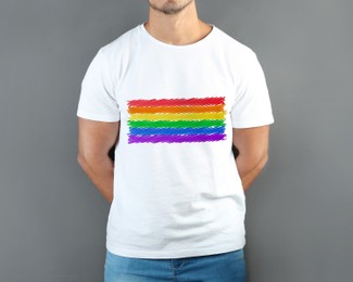 Young man wearing white t-shirt with image of LGBT pride flag on grey background