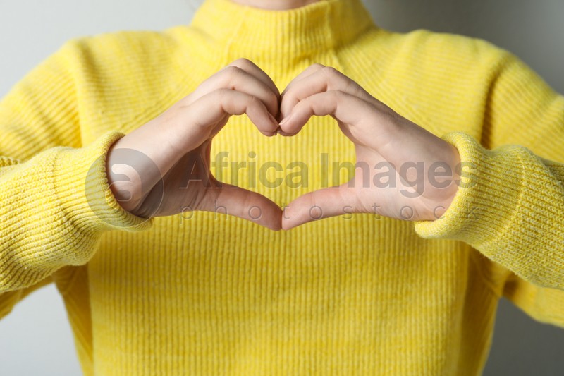 Woman making heart with her hands on light grey background, closeup