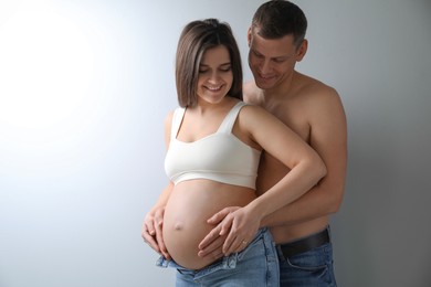 Man touching his pregnant wife's belly on light background