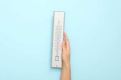 Woman with weather thermometer on light blue background, closeup