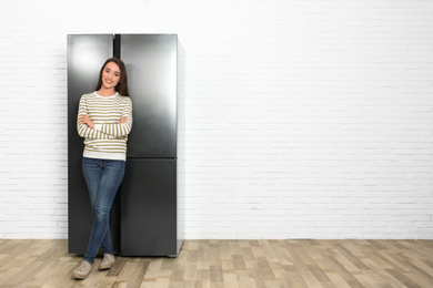 Happy young woman near refrigerator indoors, space for text