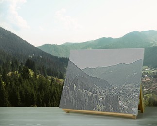 Wooden easel with picture on table and beautiful mountain landscape 