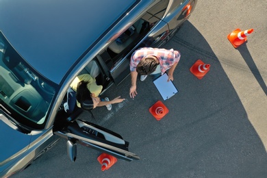 Instructor with clipboard near car and his student outdoors, above view. Driving school exam