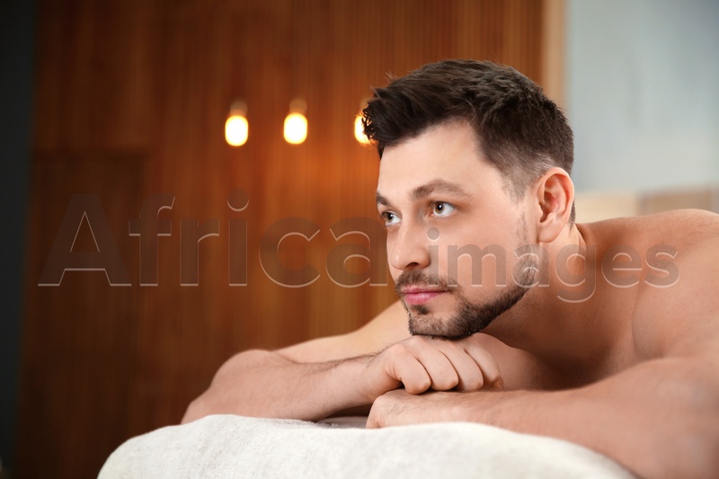 Photo of Handsome man relaxing on massage table in spa salon. Space for text