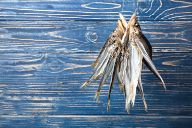 Dried fish hanging on rope against blue wooden background. Space for text