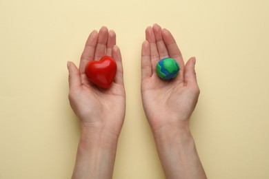 Woman holding model of planet and red heart on beige background, top view. Earth Day