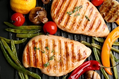Tasty grilled chicken fillets with vegetables on frying pan, flat lay