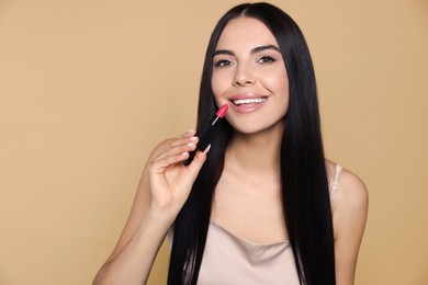 Photo of Young woman with beautiful makeup holding nude lipstick on beige background