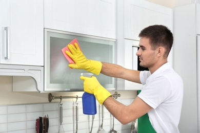 Male janitor cleaning kitchen furniture with rag in house