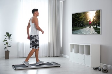 Sporty man training on walking treadmill and watching TV at home